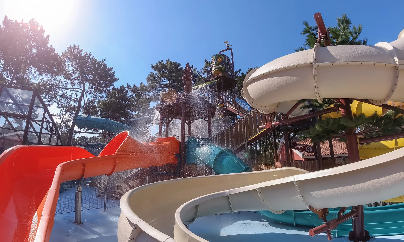 Water slides, splashing water, and trees surrounding an outdoor aquatic playground under a bright blue sky at Ohai Nazaré Outdoor Resort