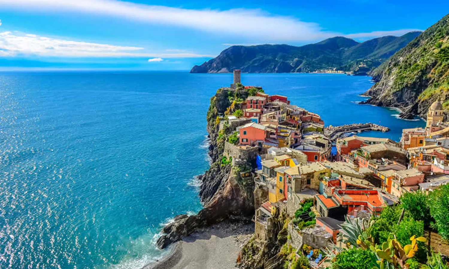 Cliffside village overlooks a stunning blue sea with lush green mountains in the background at dei Fiori