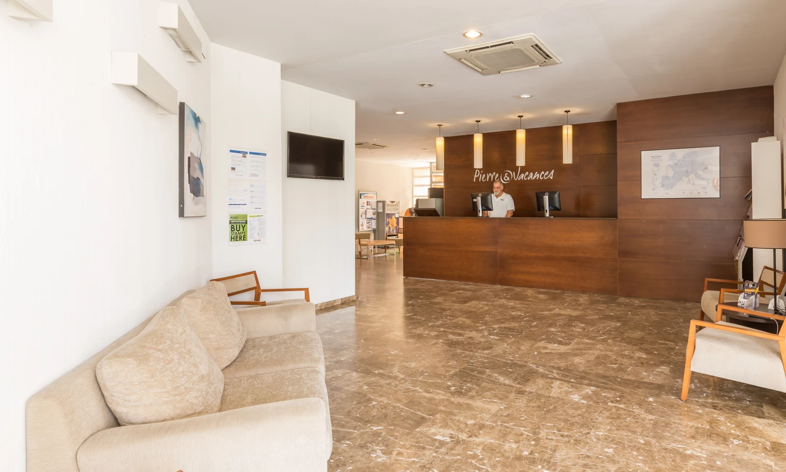 Receptionist works behind wooden desk; beige sofas and chairs line marble-floored lobby; maps and brochures on walls at Benidorm Levante