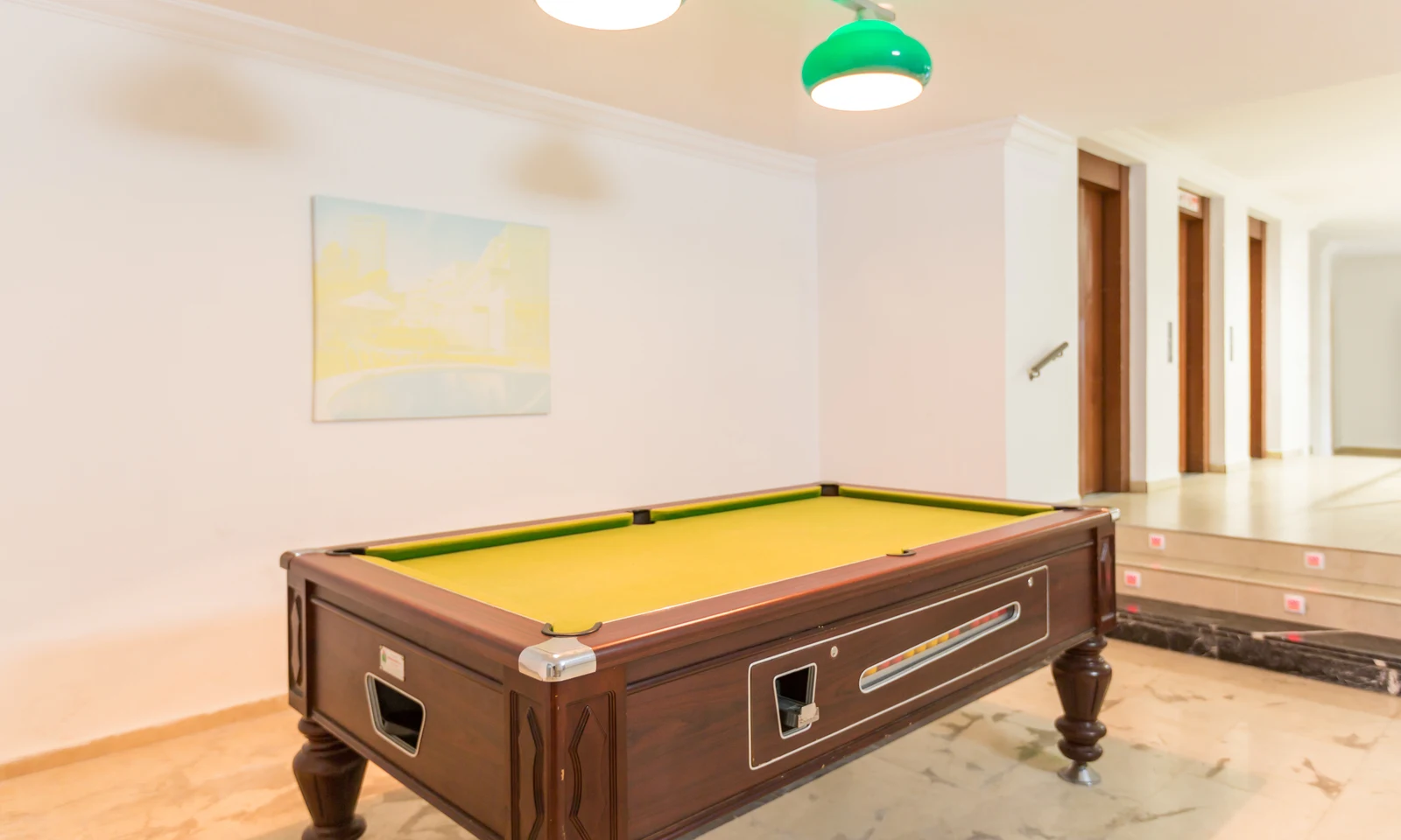 Pool table under green hanging lights in a spacious, bright room with white walls and wooden doors at Benidorm Levante