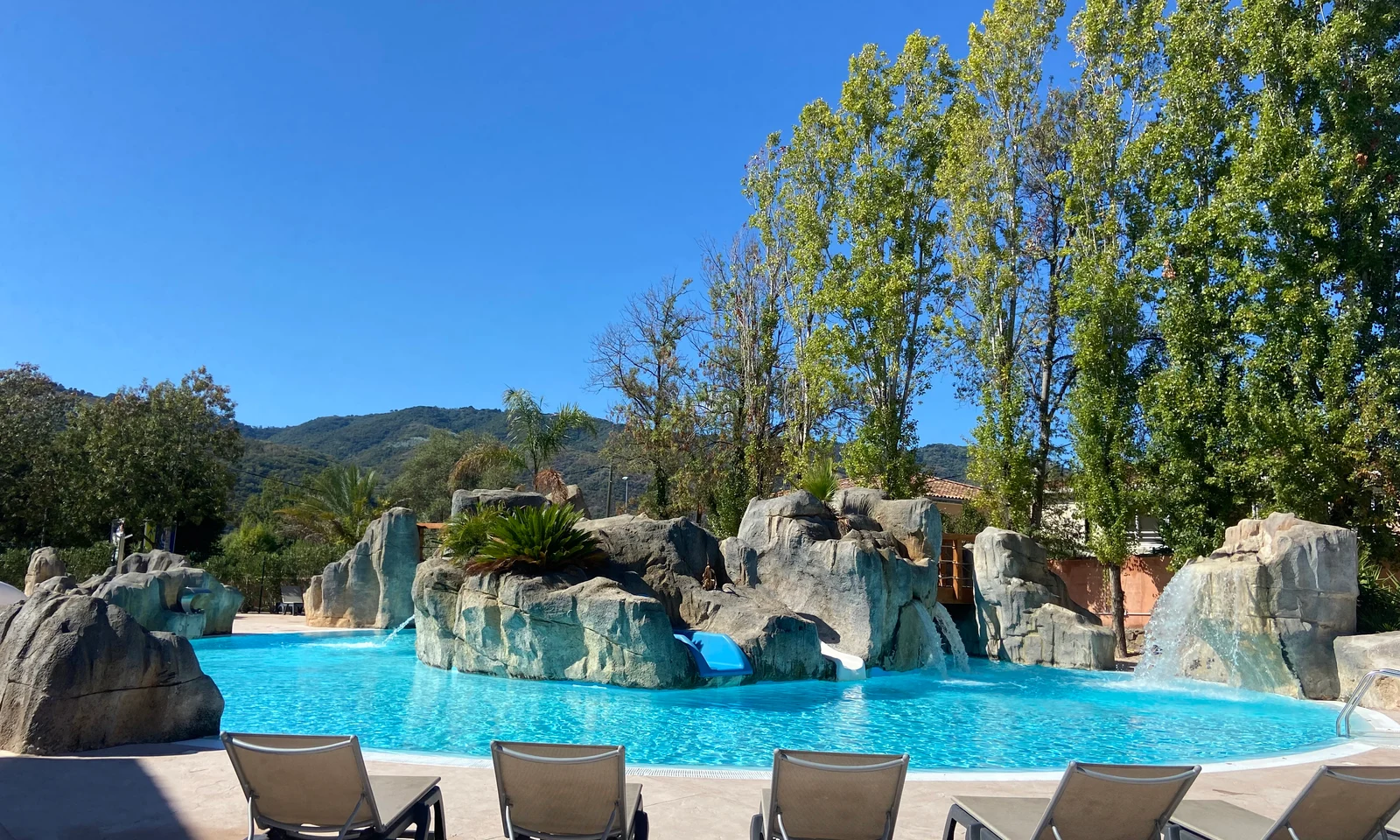Pool area with rock formations and waterfalls surrounded by lounge chairs and trees at Le Saint Louis