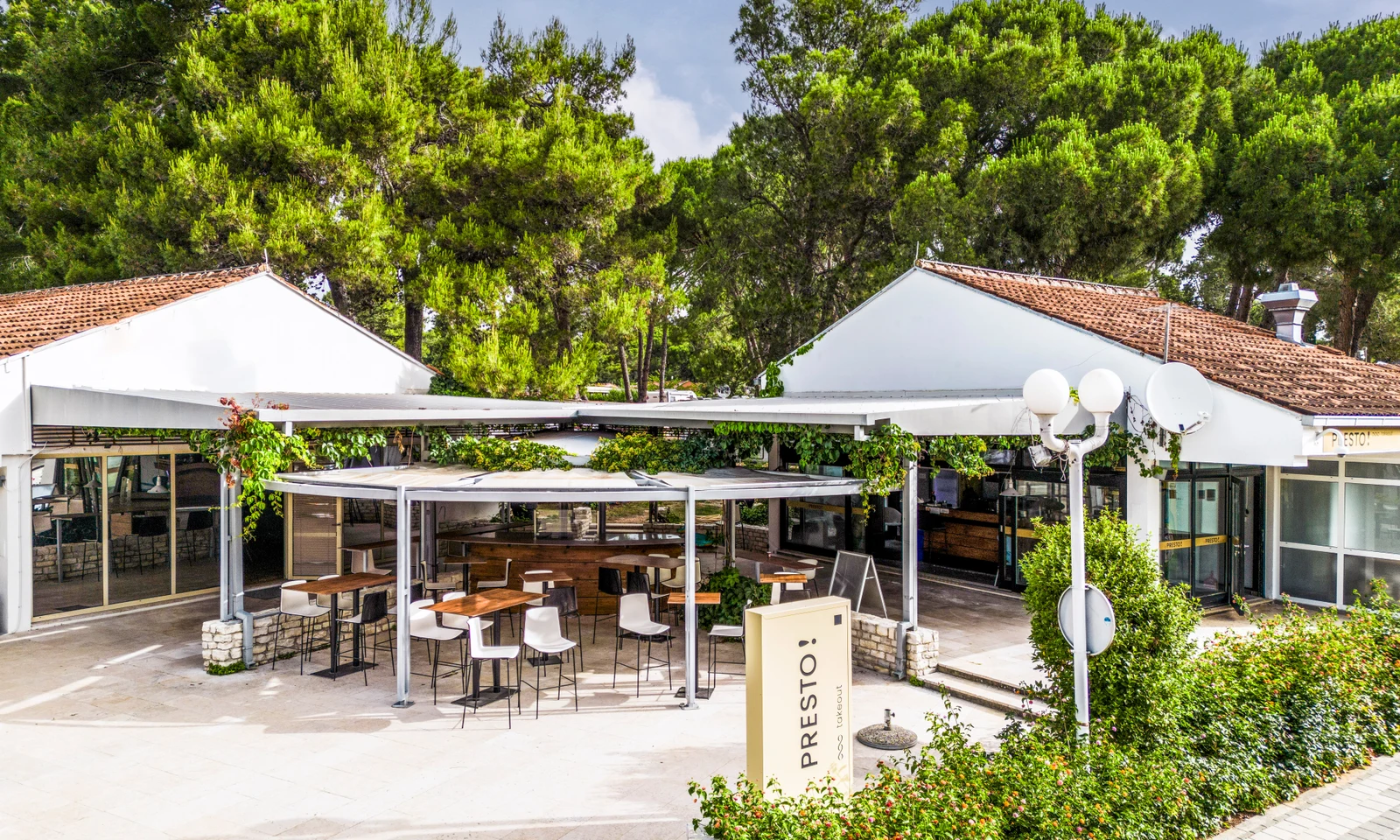 Outdoor seating area with tables and chairs under a pergola, surrounded by greenery and trees at Zaton Holiday Resort