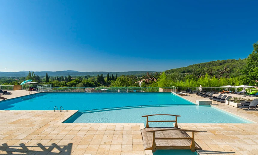 A tranquil swimming pool sits under a clear blue sky surrounded by lush green hills and lounge chairs at Residence Le Domaine de Camiole