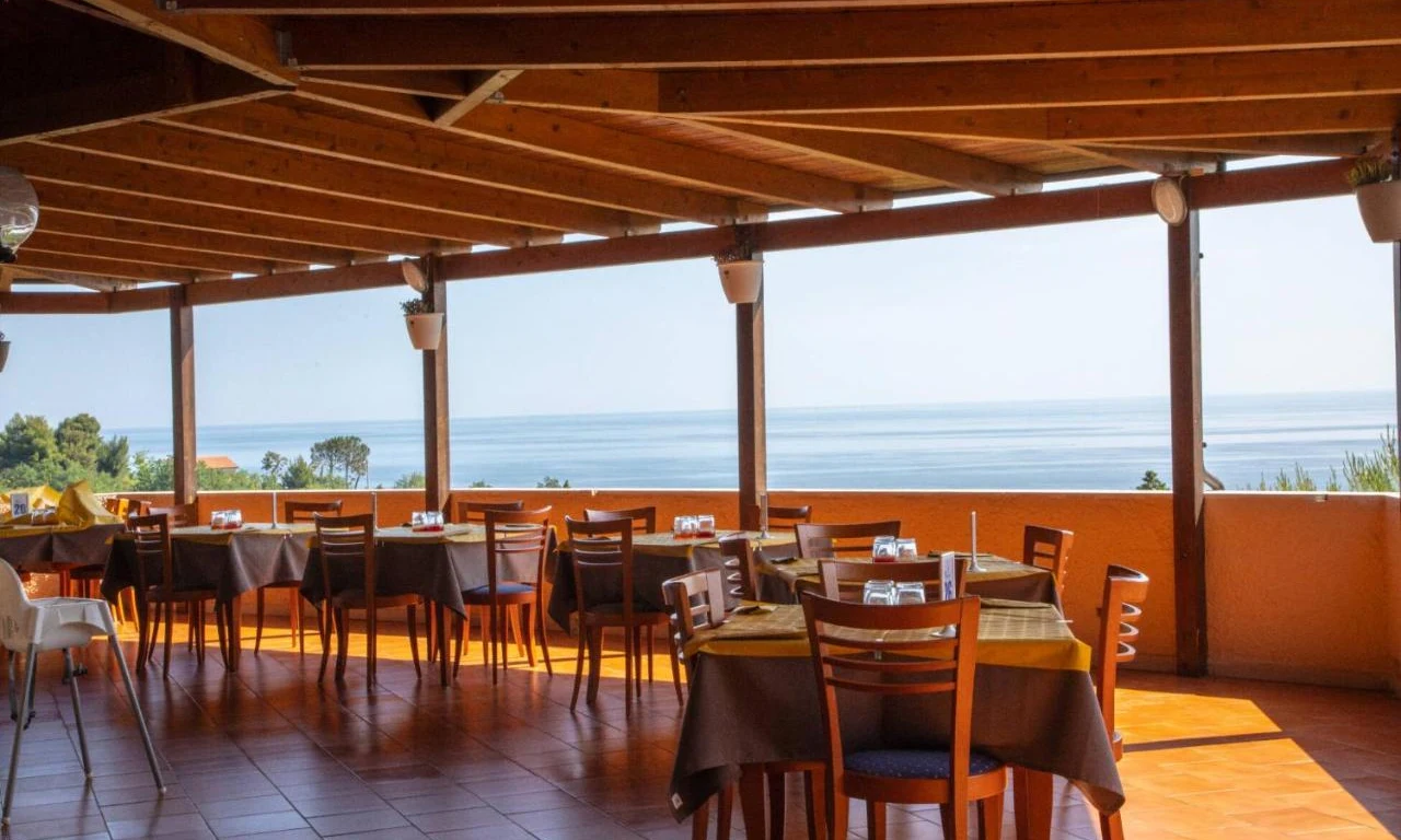 Dining tables are set under a wooden pergola, overlooking a serene ocean view; at Camping Village Mirage