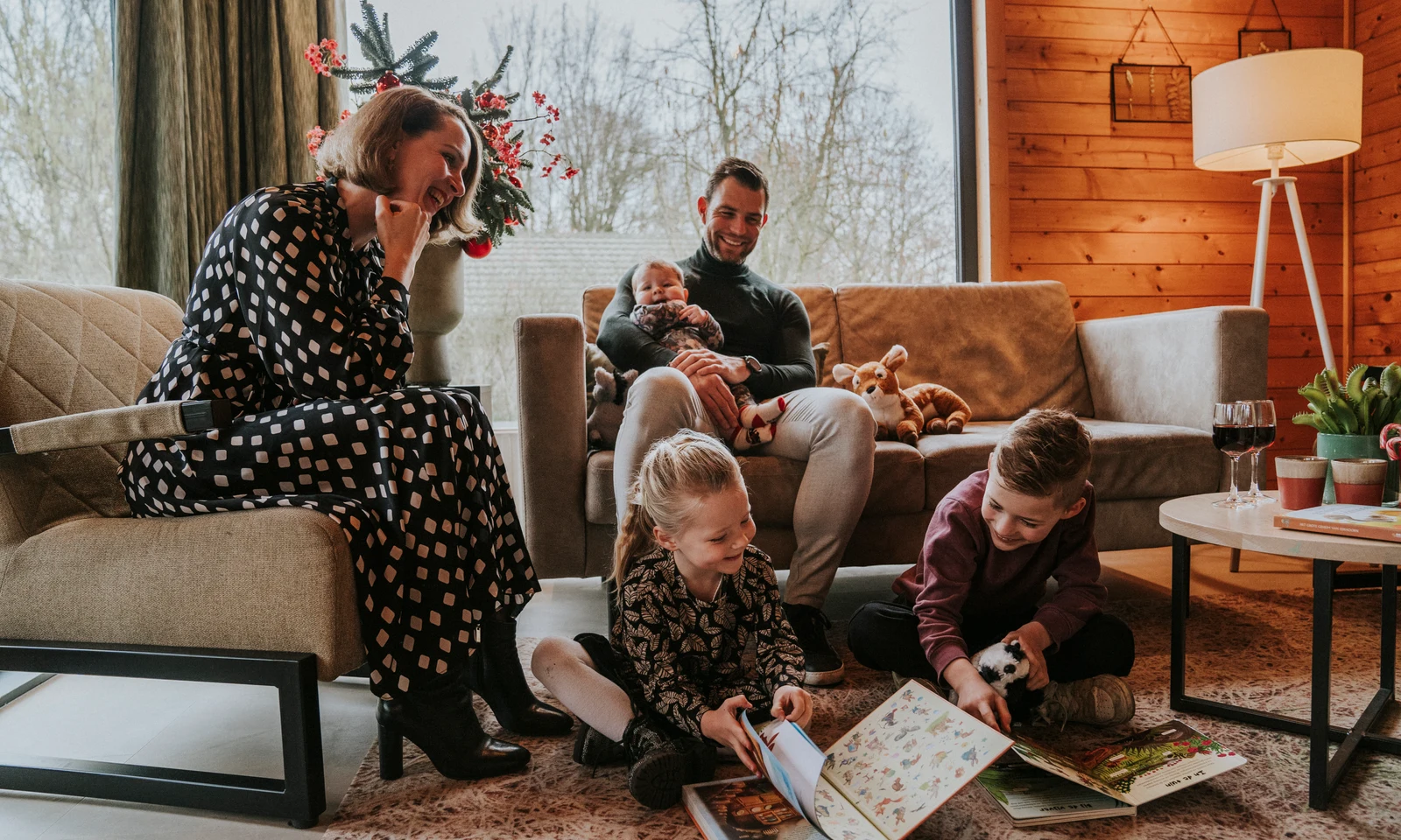 Family reading books together in a cozy wooden cabin with large windows at Vakantiepark Dierenbos