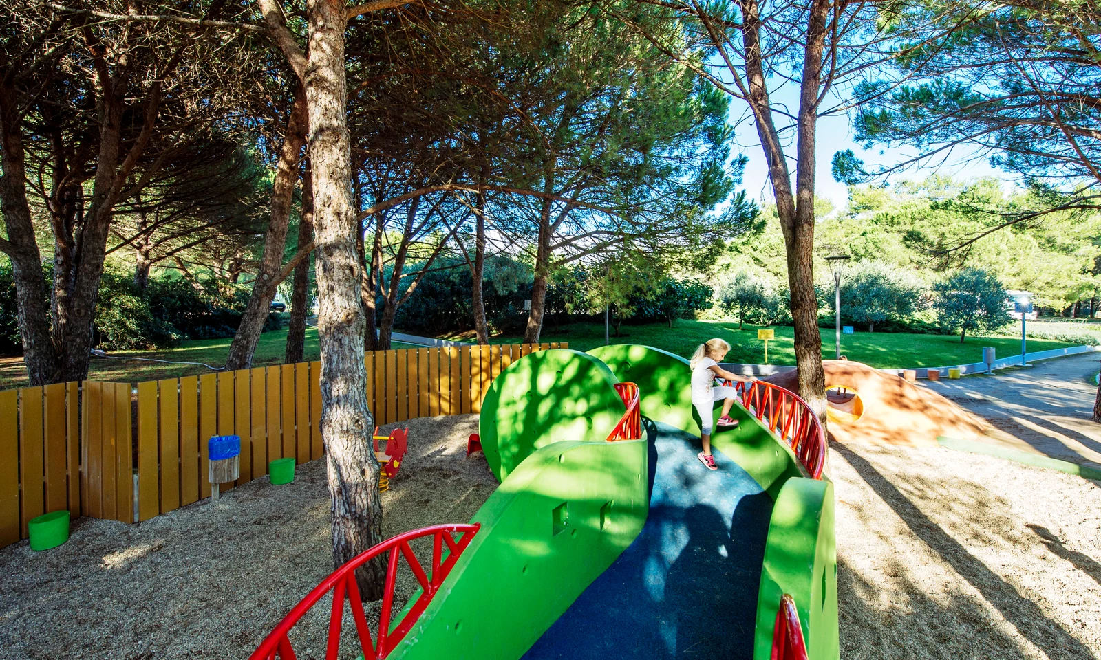 Child climbing green play structure among trees and wood fence in a sunny park at Zaton Holiday Resort