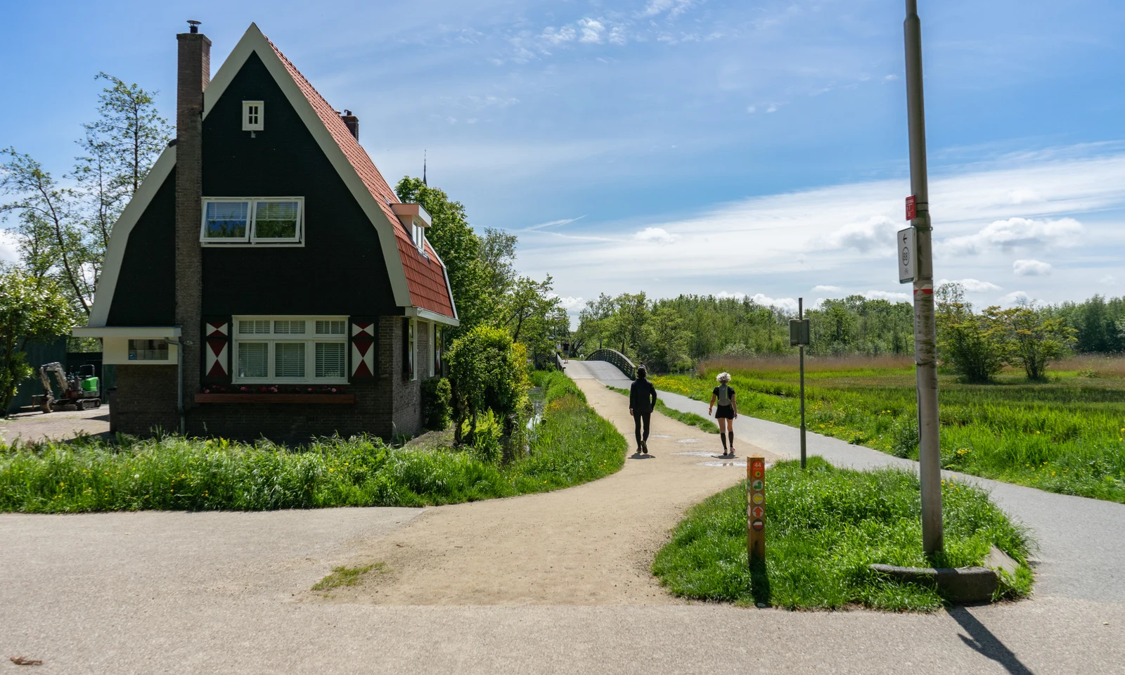 House with red roof; two people walking on path near greenery at Europarcs Het Amsterdamse Bos