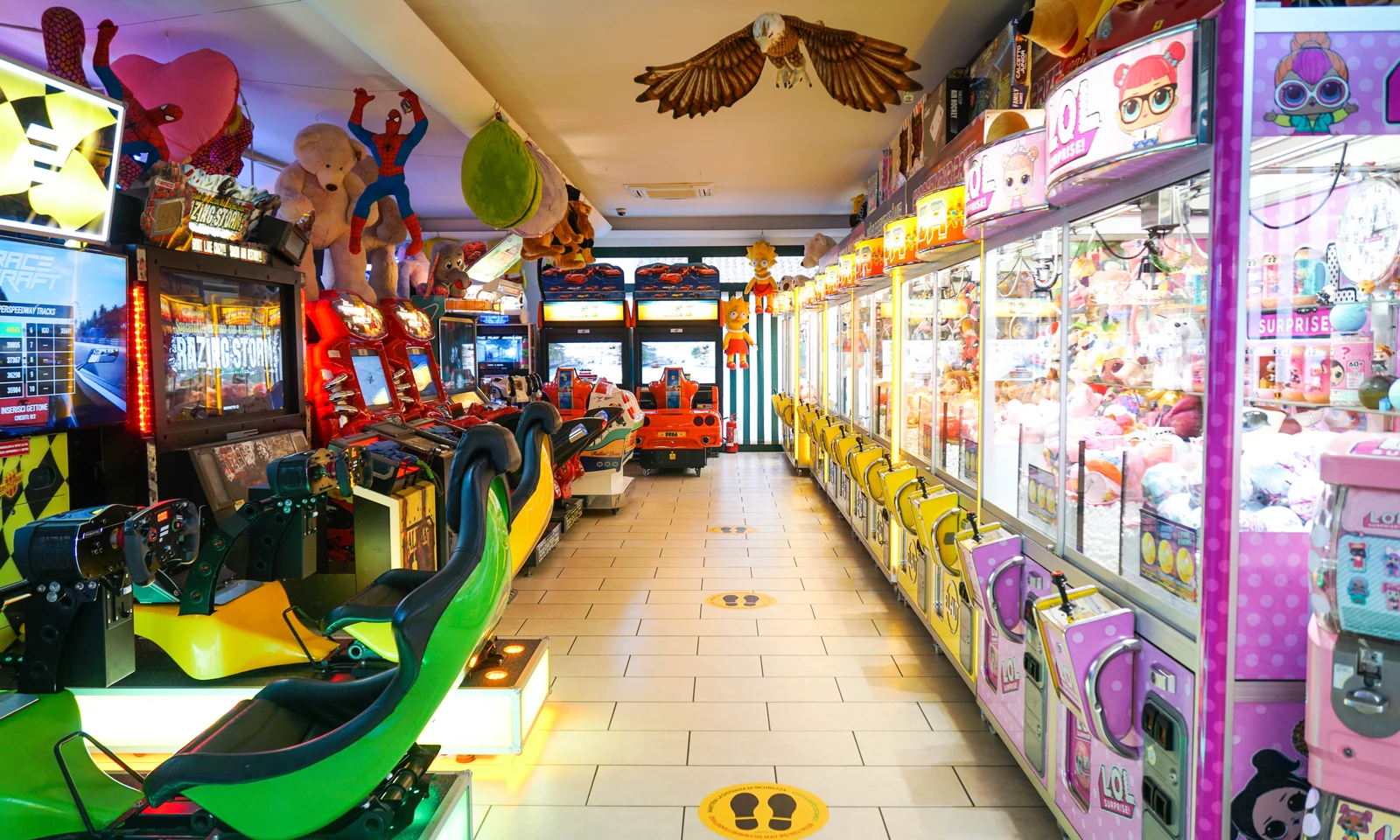 Arcade machines lined up in a colorful, indoor game center hall, with plush toys hanging above at Union Lido