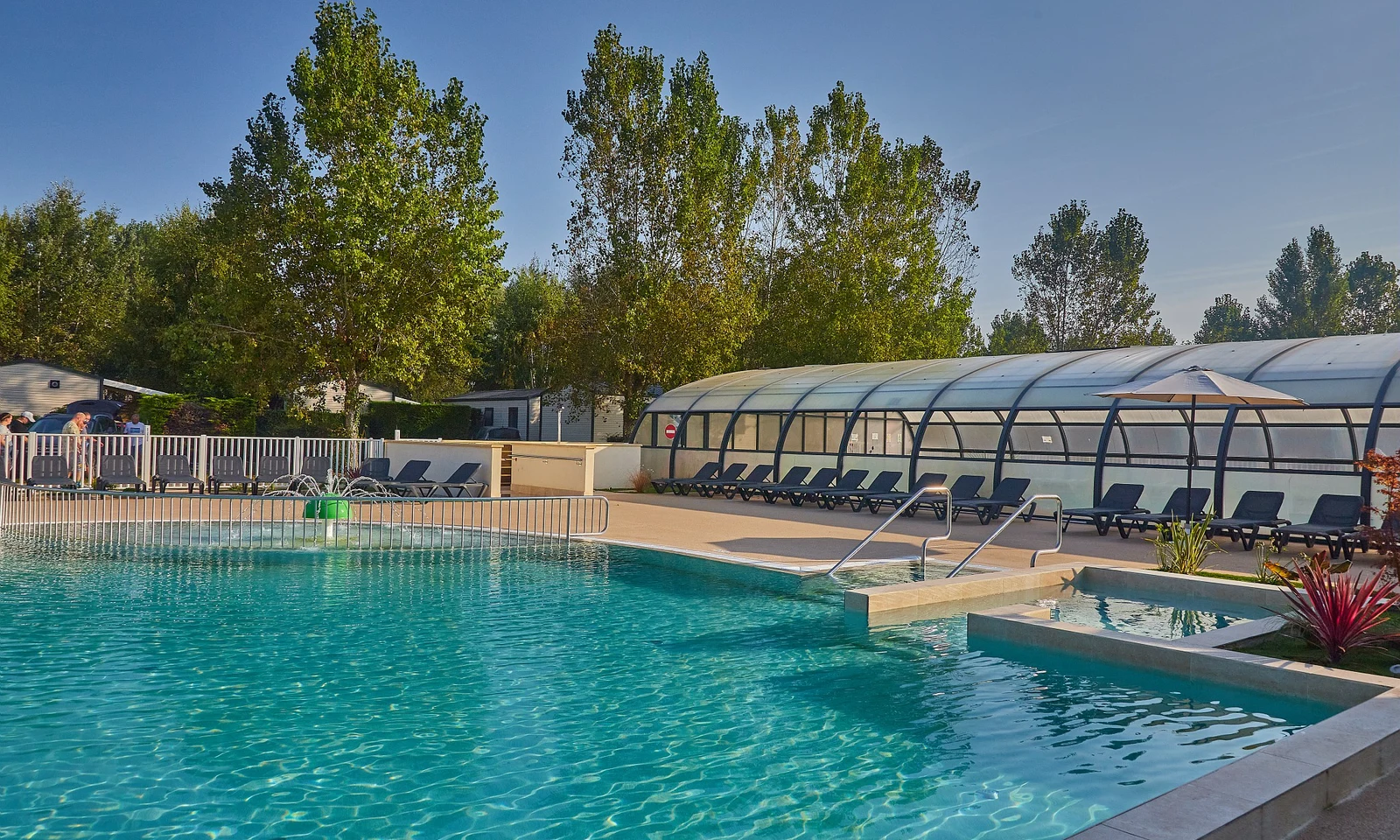 Swimming pool with clear water and nearby lounge chairs, surrounded by trees and a covered sitting area at Marvilla Parks Riva Bella