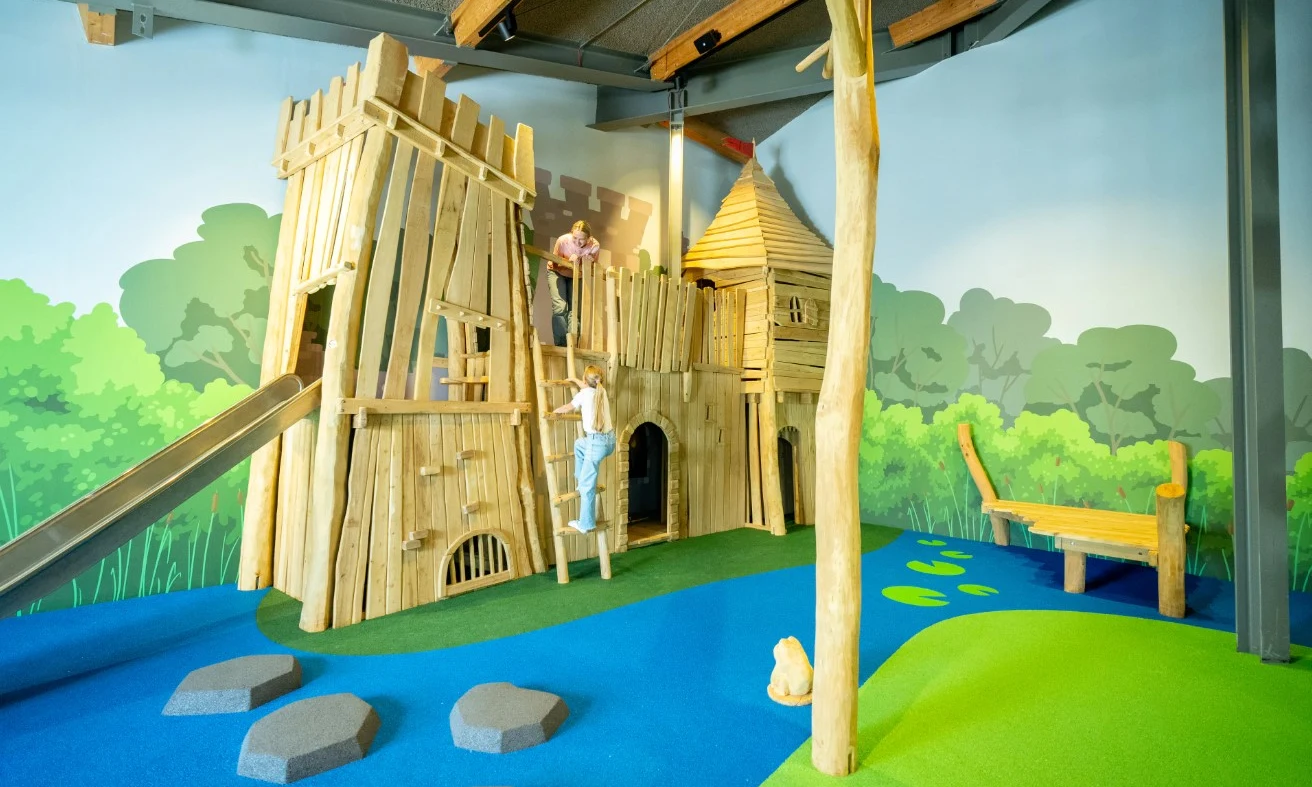 Wooden play structure with children climbing in an indoor playground, surrounded by colorful mural depicting nature at Ferienresort Cochem