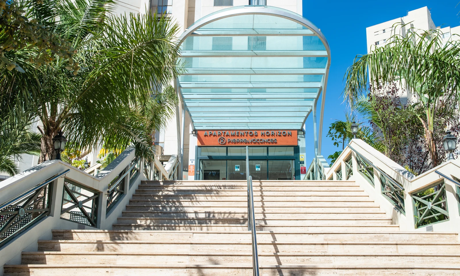 Staircase leads up to hotel entrance beneath glass canopy, surrounded by palm trees at Benidorm Horizon