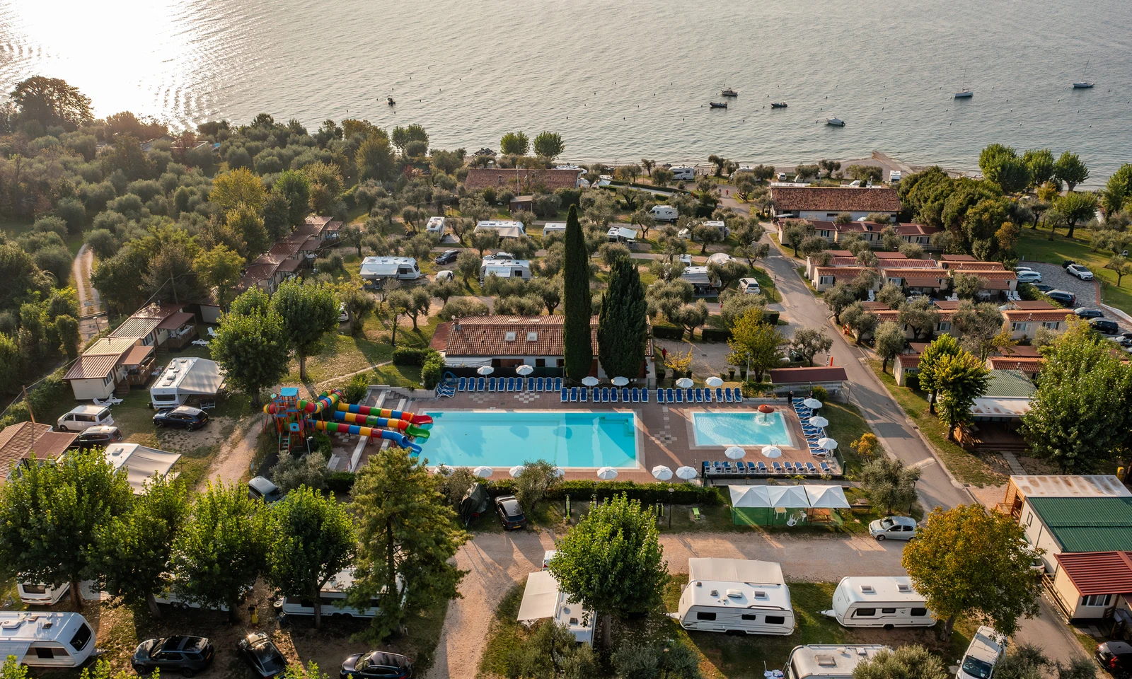 Aerial view of a campsite with a swimming pool, colorful slides, mobile homes, and trees, adjacent to a serene waterfront at Fontanelle