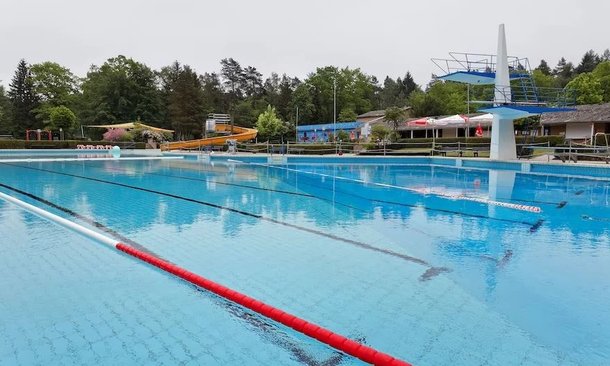 Outdoor pool with diving boards, lane markers, and a water slide in the background surrounded by trees and buildings at Knaus Campingpark Bleckede/Elbtalaue