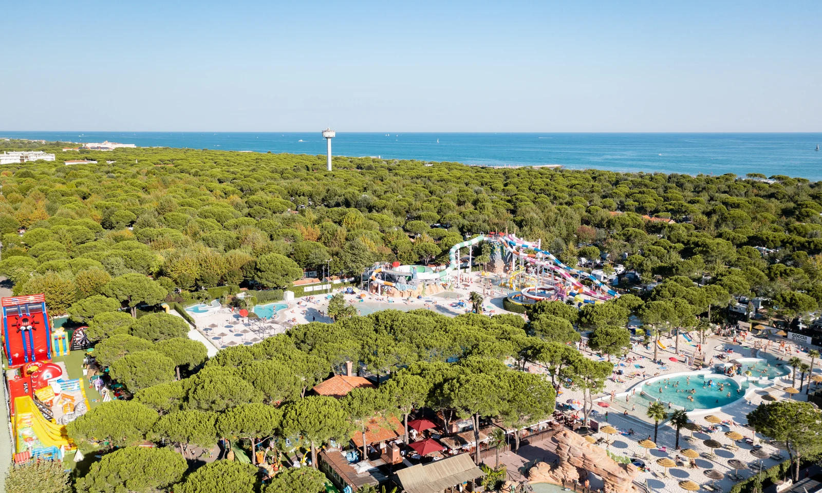 Waterpark with slides and pools bustling with visitors, set among dense green trees near a calm blue sea at Union Lido