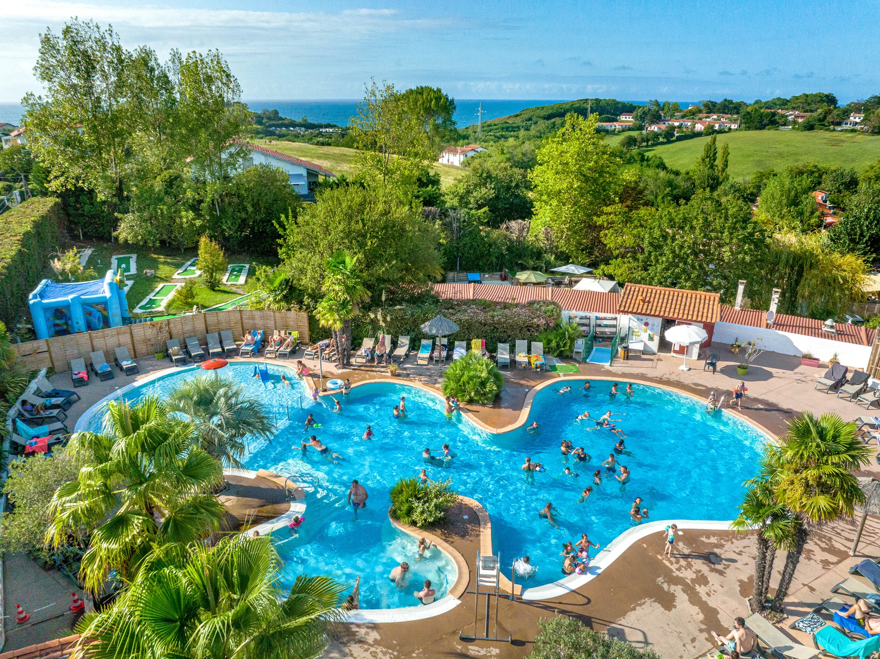 A large pool with people swimming, surrounded by lounge chairs and trees, situated near a hilly area at Atlantica