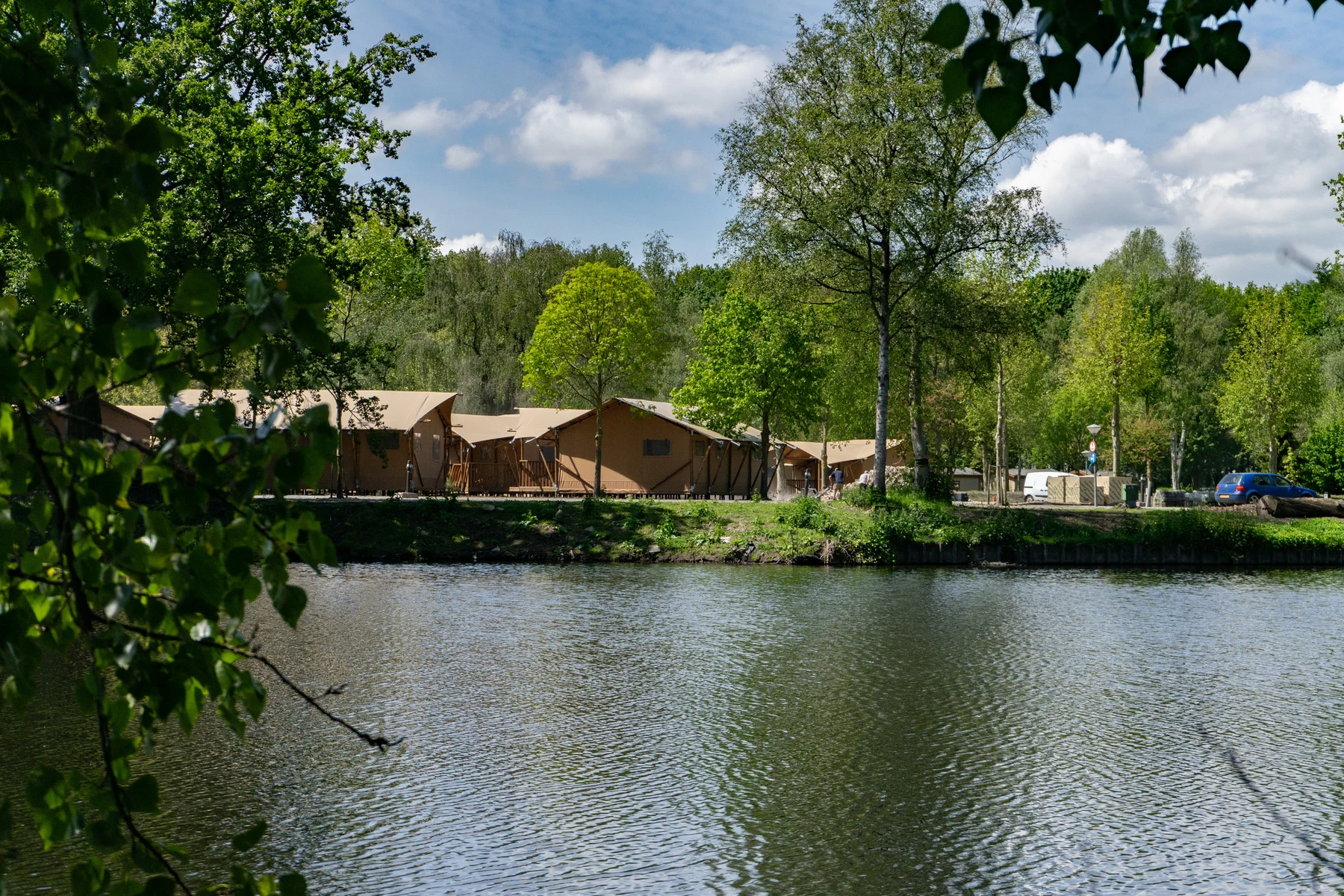 Tents lined up next to a tranquil lake and surrounded by lush trees at Europarcs Het Amsterdamse Bos
