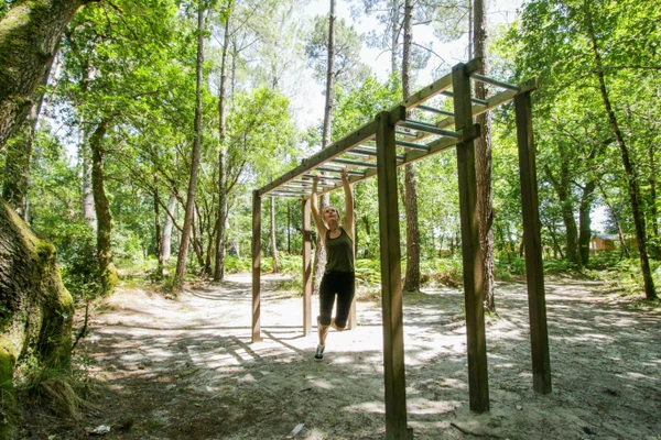 Person swinging on monkey bars in a wooded area at Au Lac de Biscarrosse