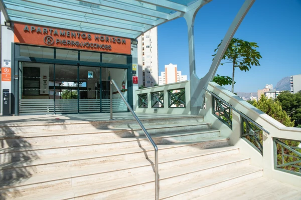 Steps leading to a glass entrance of a building with a canopy, surrounded by trees and tall buildings in the background at Benidorm Horizon