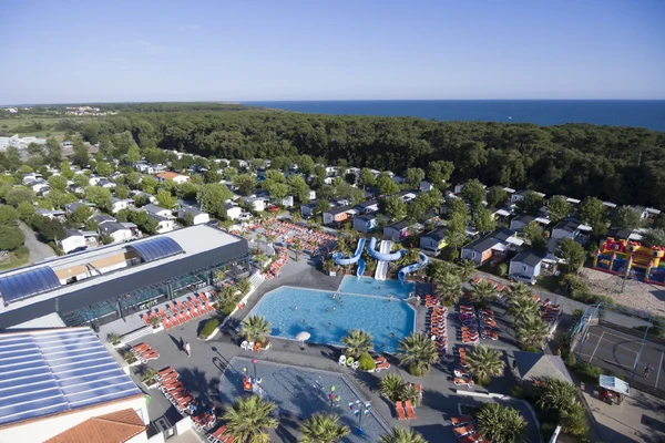 Swimming pool with slides, surrounded by sun loungers and people, amidst a camping site with numerous mobile homes near the forest and sea at Le Littoral 