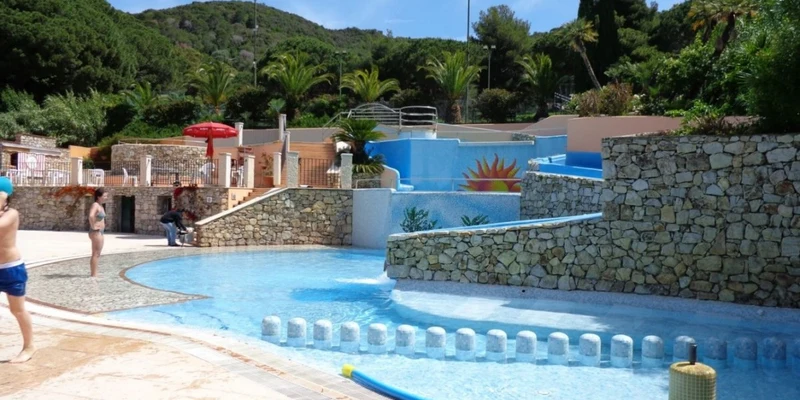 Children wading in a small, curvy swimming pool surrounded by stone walls and lush green trees at Rosselba le Palme