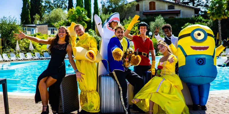 People in colorful costumes posing cheerfully by a pool, surrounded by lounge chairs and lush greenery at Europa Silvella