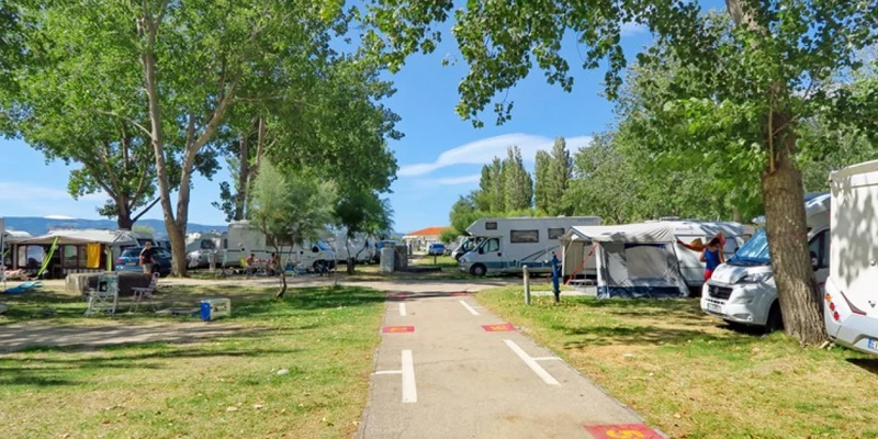 Pathway through a tree-lined campsite with parked motorhomes and tents under a clear sky at Camp Galeb