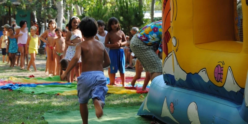 Child running toward inflatable structure while other children queue in a park with trees and grass at Molino a Fuoco