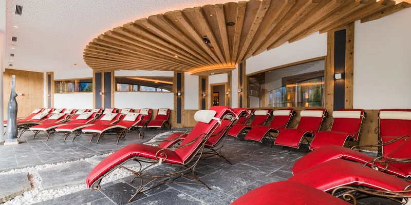 Red lounge chairs arranged under a wooden ceiling in a modern indoor recreation area at Sportcamp Woferlgut