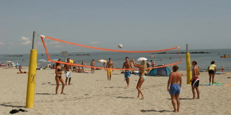 People play beach volleyball on sand with ocean and sunbathers in the background at Vigna sul Mar Family Camping Village