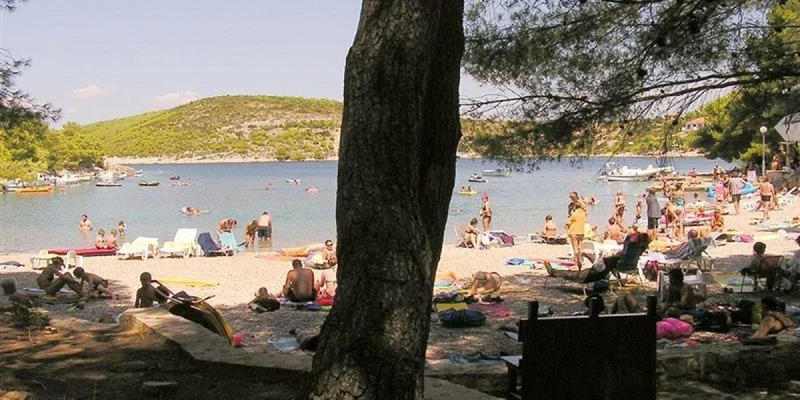 Beachgoers relaxing and swimming at a crowded beach with boats and hills in the background at Vira