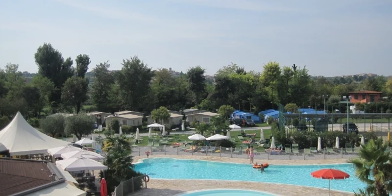 Swimming pools with sunshades and lounging chairs, surrounded by trees and camping cabins at Baia Verde