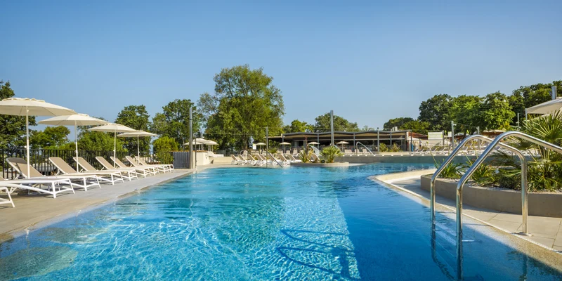 A serene blue pool surrounded by lounge chairs and umbrellas under a clear sky at Aminess Maravea Camping Resort