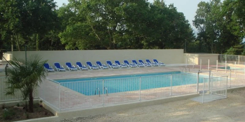 Swimming pool surrounded by lounge chairs sits in a fenced area with trees in the background at La Buissière 