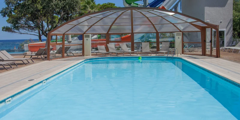 Swimming pool surrounded by lounge chairs and covered area, with a large waterslide and trees in the background at Merendella