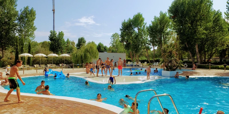 People of all ages enjoy swimming in an outdoor pool surrounded by trees and lounge chairs at Molino a Fuoco