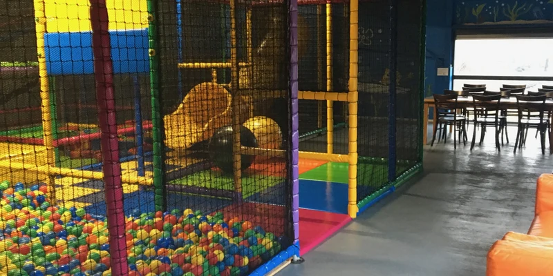 Indoor playground with colorful climbing structures and ball pit, near orange sofas and dining area at Lauwersoog