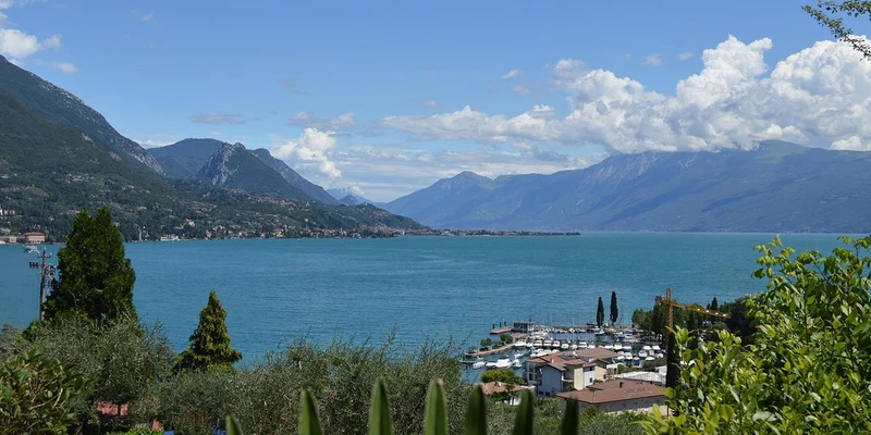 Lake bordered by mountains, boats docked at a marina, lush greenery in foreground, blue sky with clouds at Eden