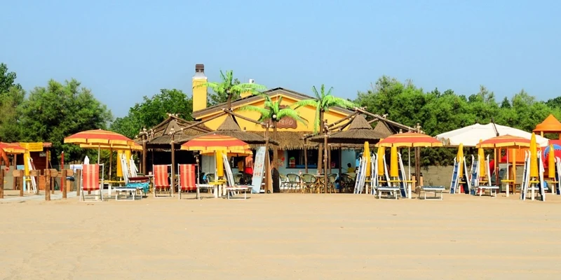 Beach cafe with colorful umbrellas and lounge chairs, surrounded by lush greenery under a clear blue sky at Spiaggia e Mare