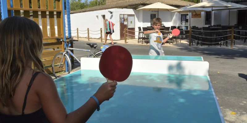 Two people playing table tennis outdoors near a building with tables and umbrellas at Maïana Resort