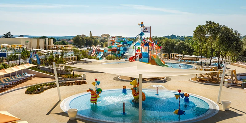 Brightly colored water park with slides and pools, bustling with activity, surrounded by loungers and trees at Valamar Camping Istra