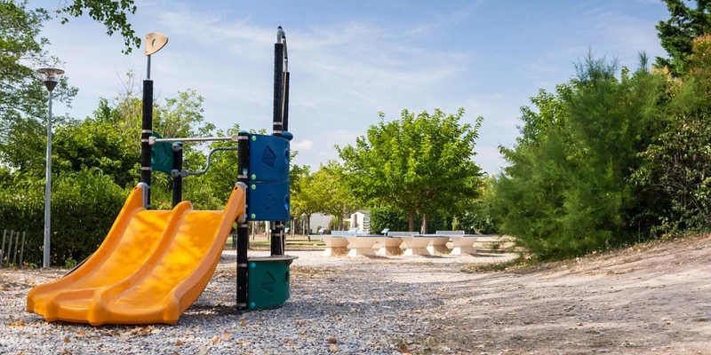 Bright orange slide stands still beside green trees at Marvilla Parks Les Rives du Luberon