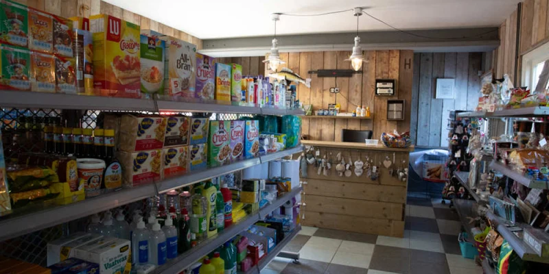 Shelves stocked with groceries and cleaning supplies in a small wooden shop with a checkered floor at Europarcs De Biesbosch