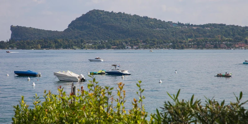 Boats floating on a calm lake with a mountainous backdrop, bordered by leafy green vegetation in the foreground at La Gardiola
