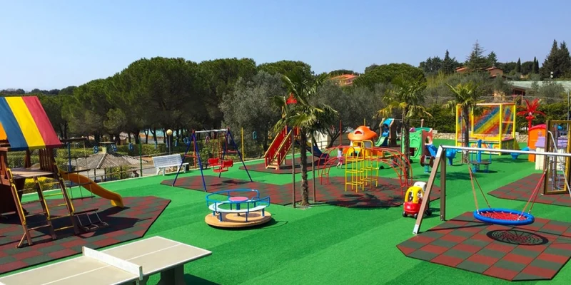 Playground with colorful equipment, including slides and swings, amidst trees and greenery at Valle Gaia