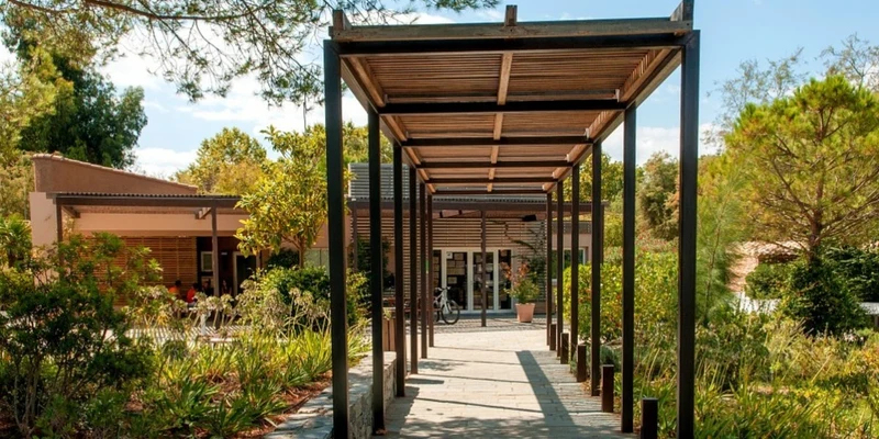 Wooden pergola stretches over a stone-paved pathway, leading to a building surrounded by lush greenery at Marina d'Erba Rossa