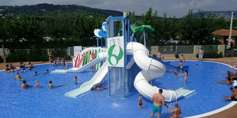 Water slide tower with children playing in a shallow pool, surrounded by adults under a cloudy sky at Eurocamping