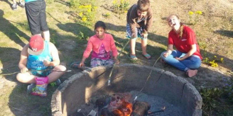 Four children roasting marshmallows around a campfire in an outdoor setting on a sunny day at Vlugtenburg