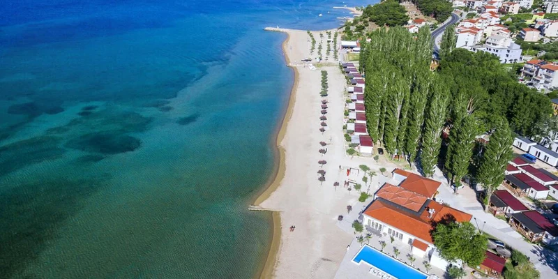 Aerial view of beachfront lodges, orderly umbrellas; vibrant town in the background at Camp Galeb