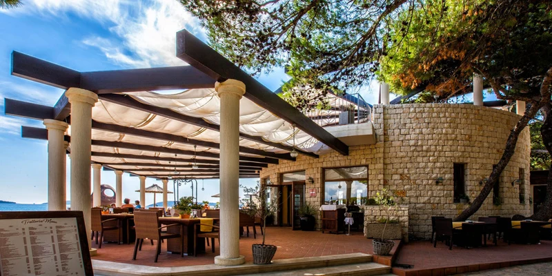 Restaurant with outdoor seating beneath a canopy, surrounded by stone walls and trees at Amadria Park Camping Sibenik 