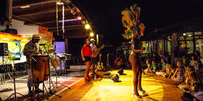 Musicians performing and a dancer in feathered costume entertaining audience seated around stage at night at Belvedere Pineta